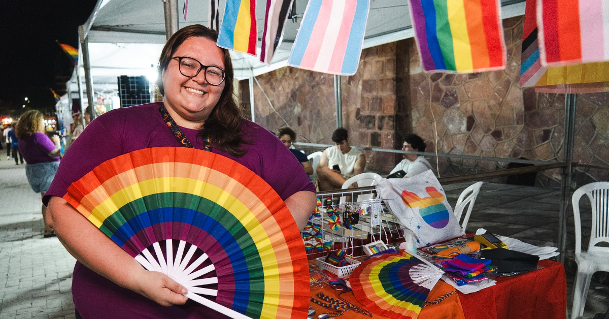 Thalyne standing in front of a market stall holding a rainbow fan