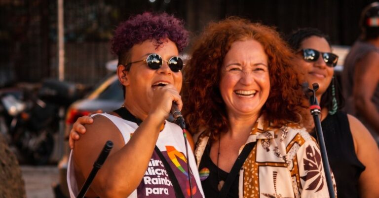 A mixed race woman with short curly brown hair, stood next to a white woman with long curly hair.